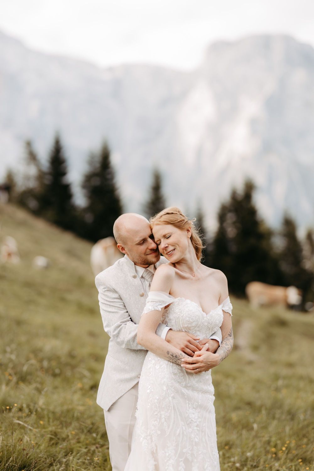 Ein Paar in Hochzeitskleidung umarmt sich glücklich auf einer Bergwiese, umgeben von Natur und Bergen – Berghochzeit auf der Tiergartenalm, Mühlbach