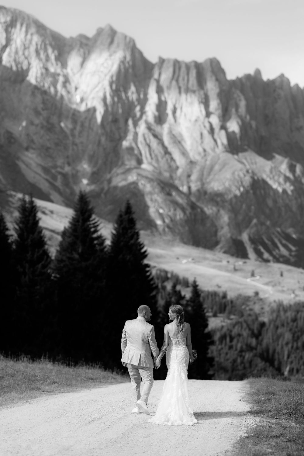 Ein Paar in Hochzeitskleidung geht einen Weg entlang, umgeben von majestätischen Bergen, symbolisiert gemeinsame Lebensreise – Berghochzeit auf der Tiergartenalm, Mühlbach