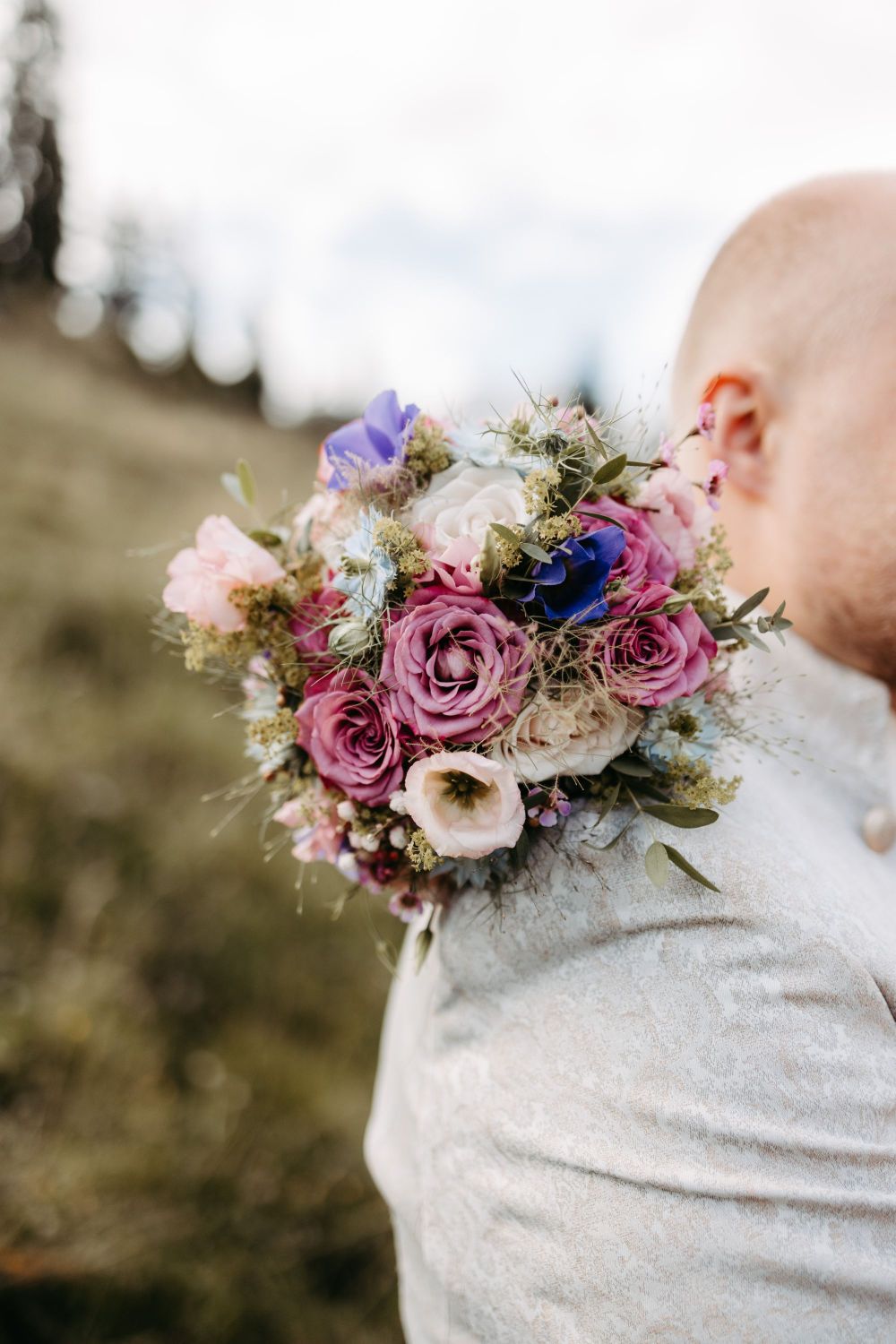 Ein Mann mit Blumenstrauß auf der Schulter in der Natur, Symbol für Neuanfang und persönliche Entwicklung – Berghochzeit auf der Tiergartenalm, Mühlbach