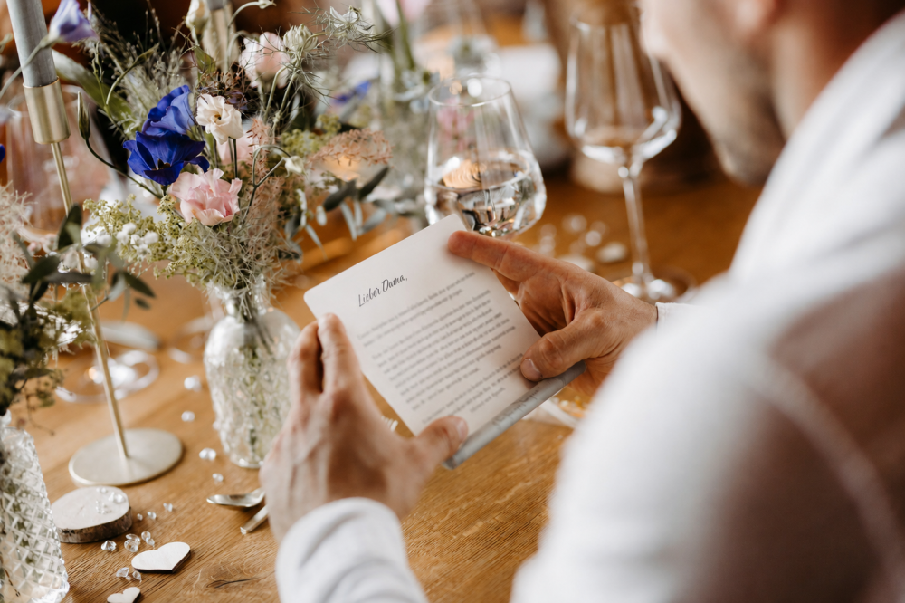 Person liest einen Brief an einem dekorierten Tisch mit Blumen und Kerzen, fördert Reflexion und persönliche Entwicklung.