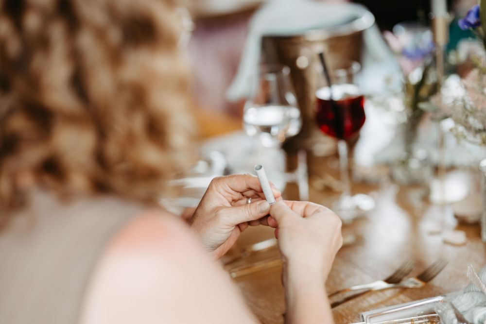 Person rollt Papier in entspannter Umgebung, Glas Wein im Hintergrund. Symbolisiert Fokus und Achtsamkeit – Berghochzeit auf der Tiergartenalm, Mühlbach