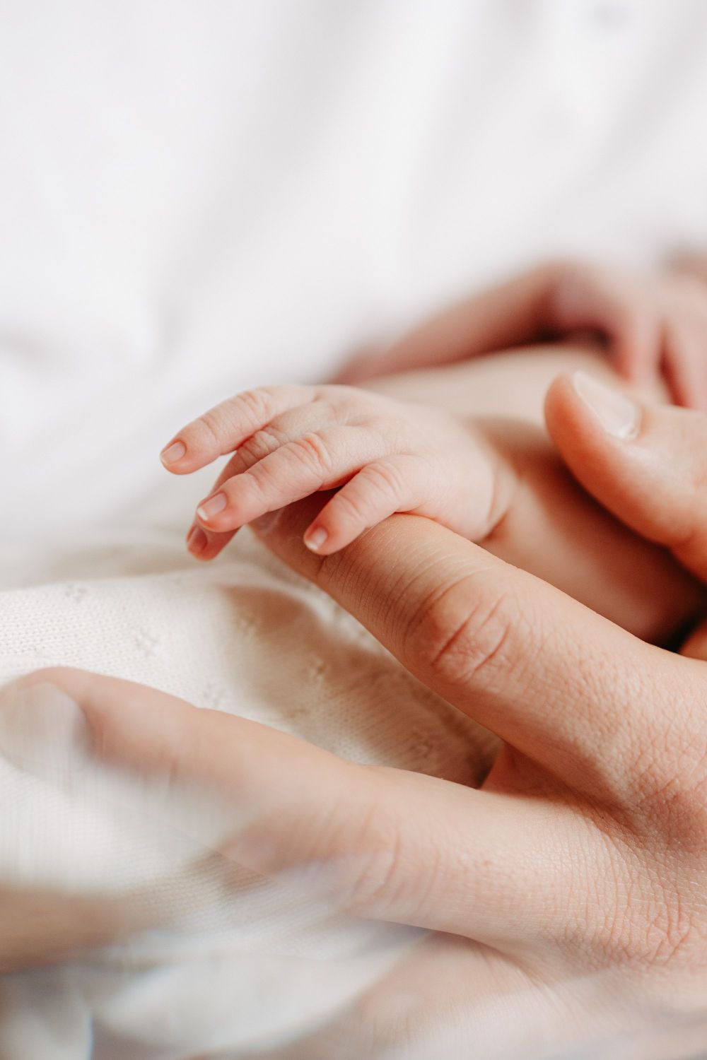 Nahaufnahme einer Babyhand, die den Finger eines Erwachsenen hält. Hintergrund ist weich und unscharf.