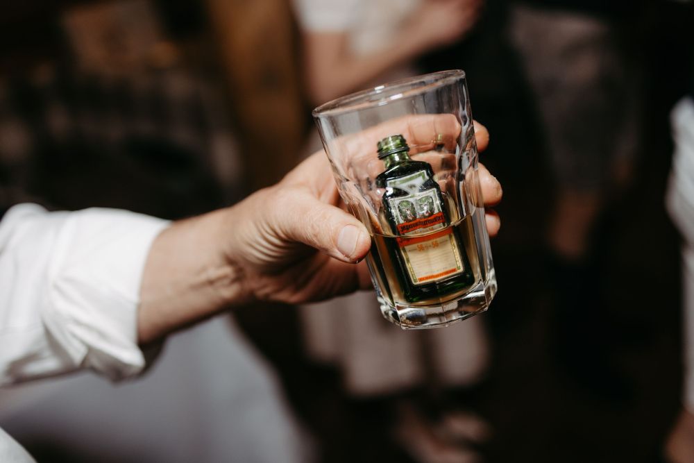 Eine Hand hält ein Glas, in dem sich eine kleine, grüne Flasche mit Etikett befindet.