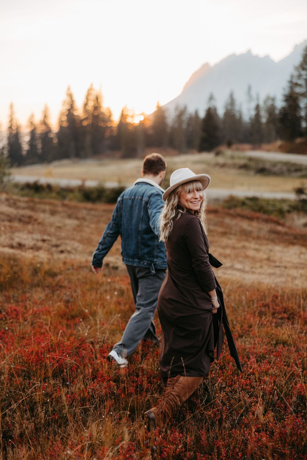 Paar spaziert bei Sonnenuntergang durch eine Herbstlandschaft. Frau lächelt in die Kamera, inspiriert zur Selbstentfaltung.