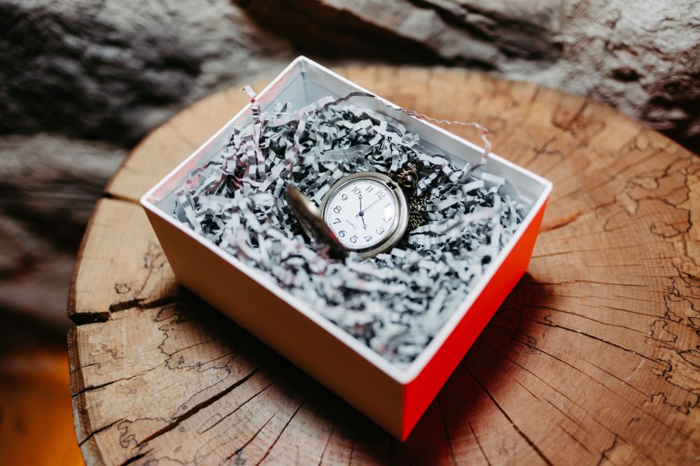 Eine Taschenuhr in einer Geschenkbox auf Holz. Symbol für Zeit und Selbstentfaltung – Berghochzeit auf der Tiergartenalm, Mühlbach