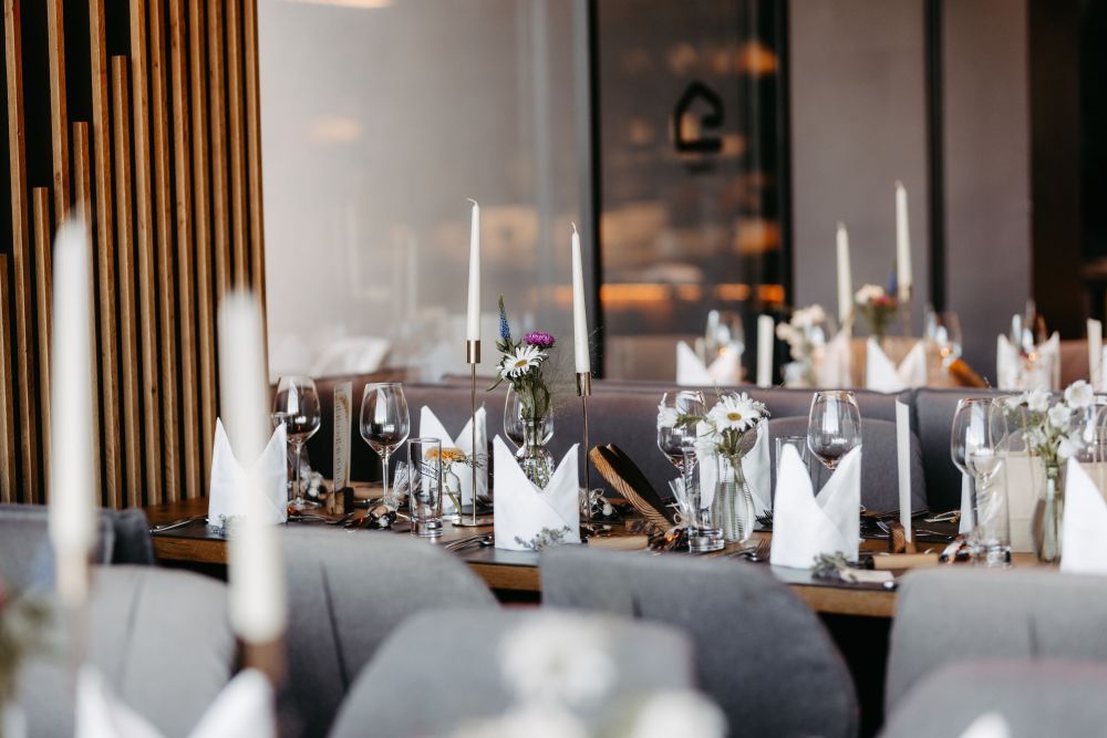 Elegante, gedeckte Tafel mit Blumen, Kerzen und Gläsern in einem stilvollen Restaurantambiente.