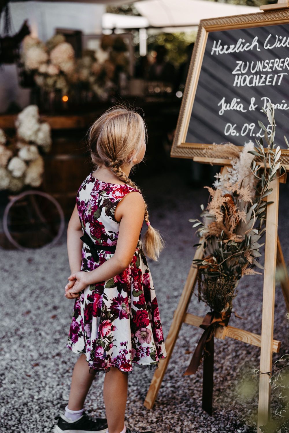Mädchen im geblümten Kleid betrachtet eine Hochzeitstafel mit Blumenarrangement.